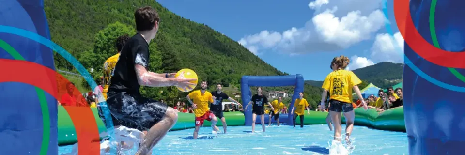 Students playing soap football in a swimming pool, mountains in background
