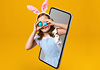 Bambina con orecchie di coniglio e binocolo che esce da uno smartphone