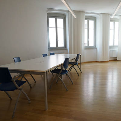 well-lit room with windows, white table and blue chairs