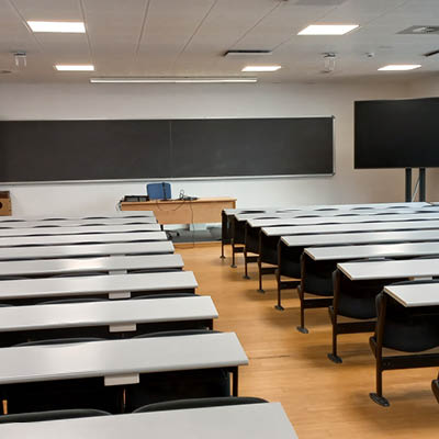 large room with rows of desks and chairs, large blackboard and monitor