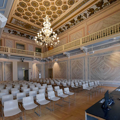 large hall with upper balcony, white chairs, marble walls and frescoes