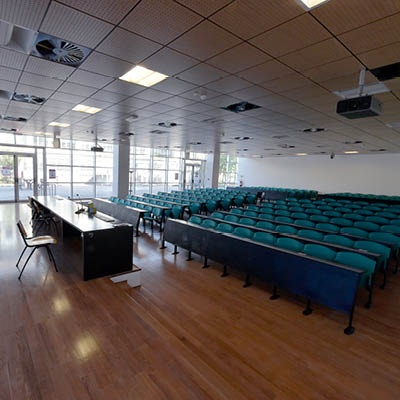 lecture theatre with rows of desks and green chairs on wooden floor
