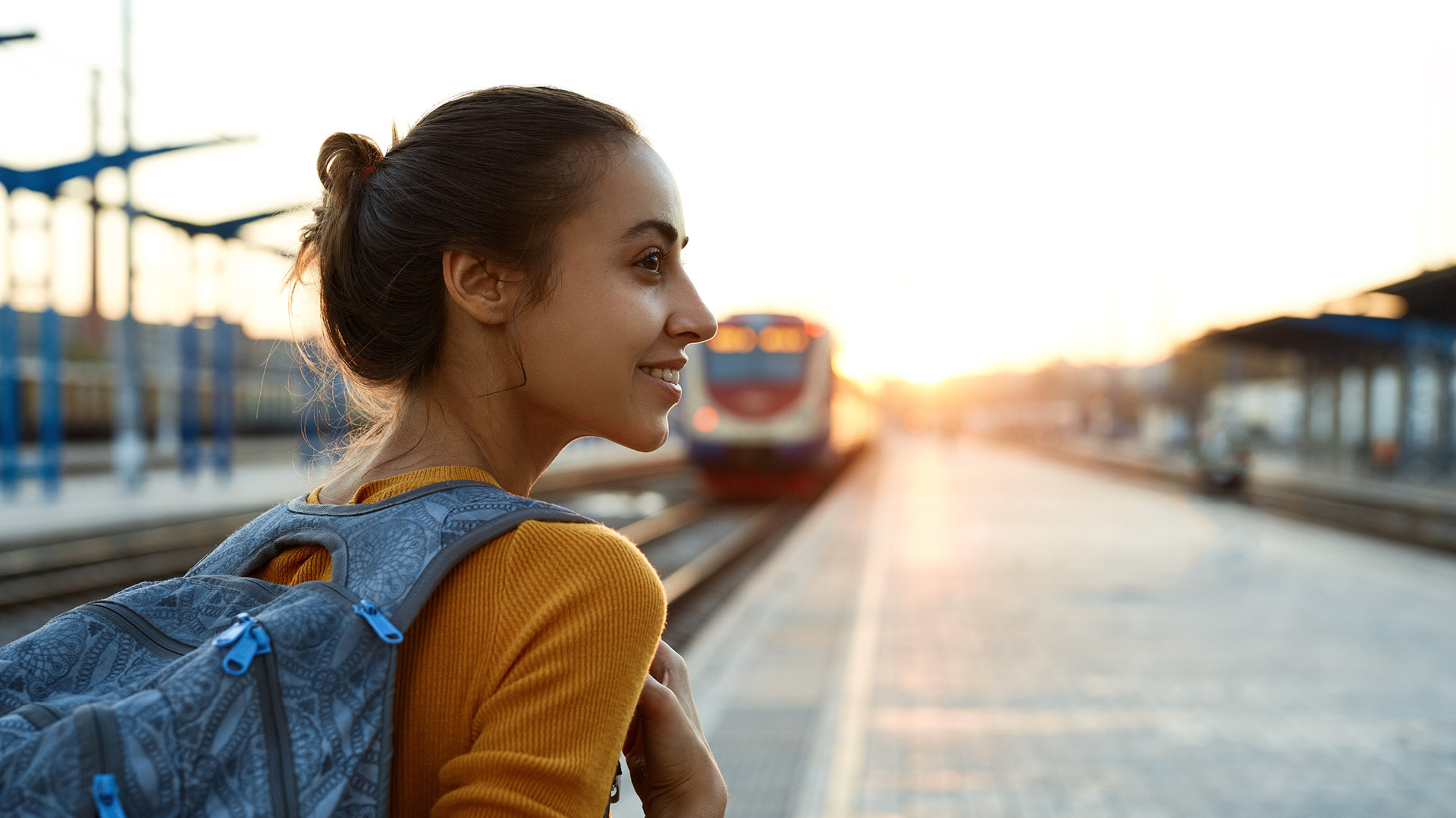 ragazza con zaino vicino a ferrovia con treno sullo sfondo