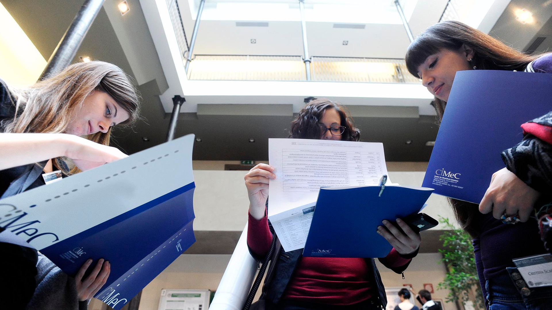 studenti con cartellette e documenti cartacei con logo CIMEC