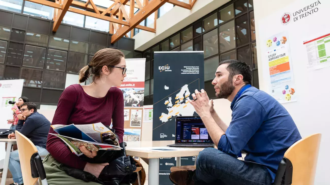 ragazza seduta ad uno stand informativo con personale di staff
