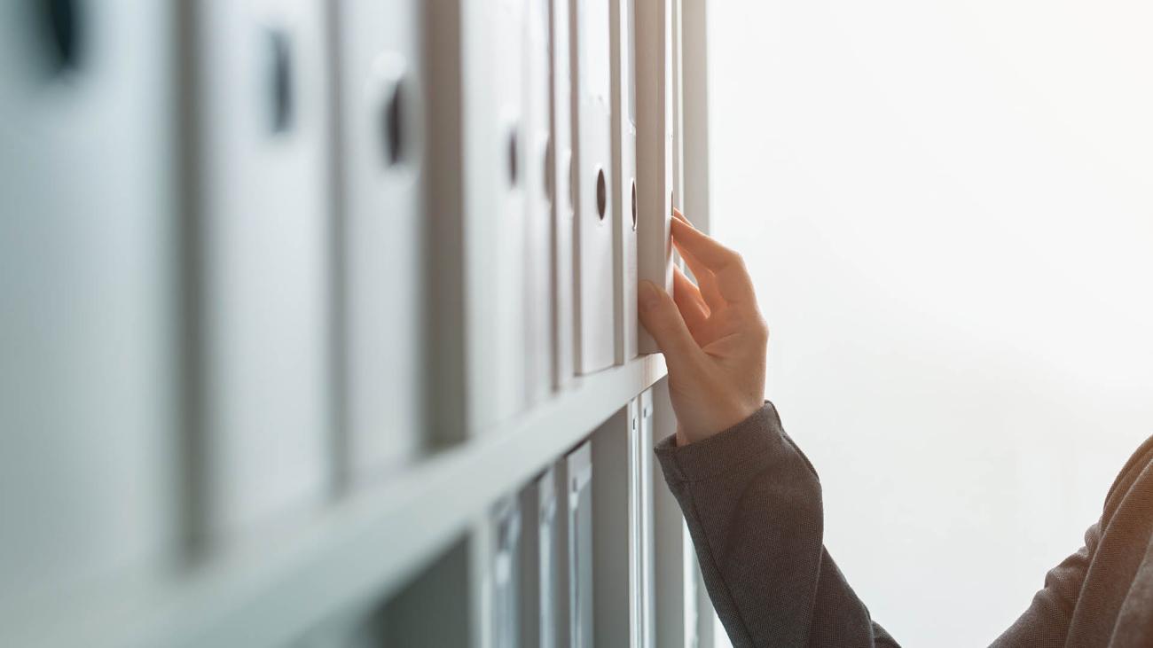 mano che estrae un raccoglitore di archivio da una libreria