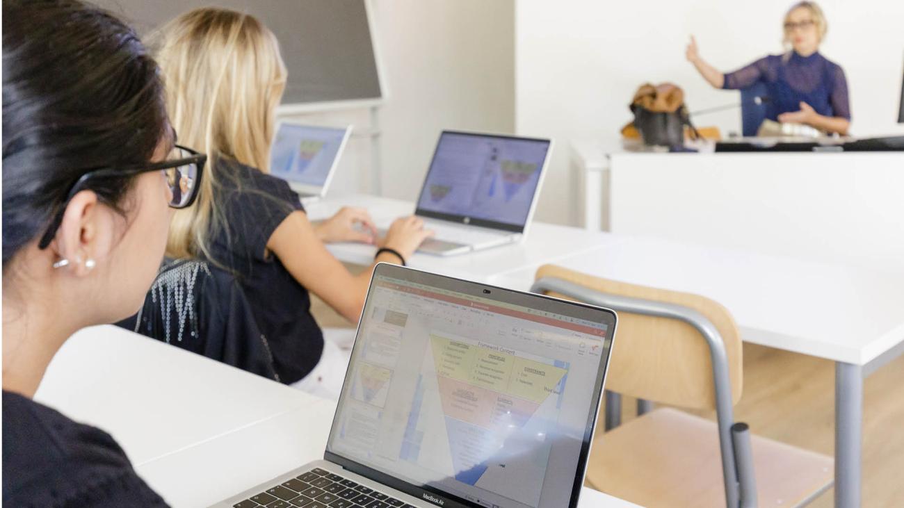 persone in aula con laptop e docente sullo sfondo