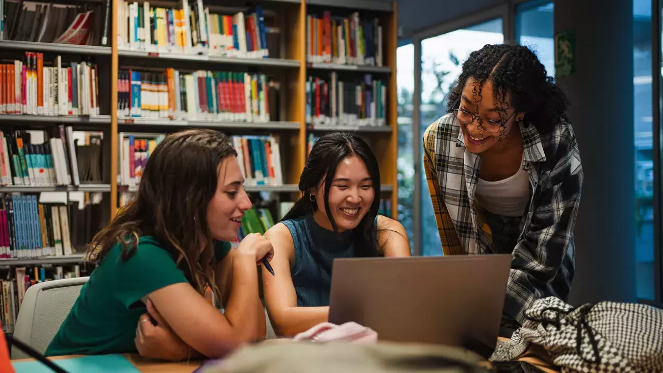 gruppo di studenti internazionali davanti a laptop con libreria sullo sfondo