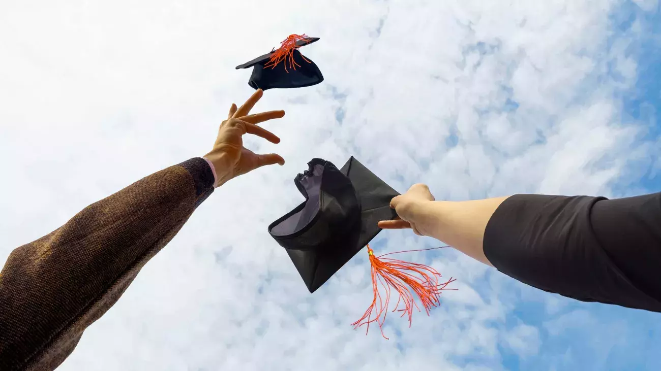 mani che lanciano in alto il tocco del laureato, cielo azzurro