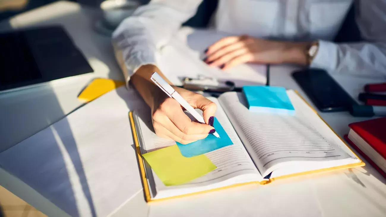 mani che scrivono su agenda, post-it colorati